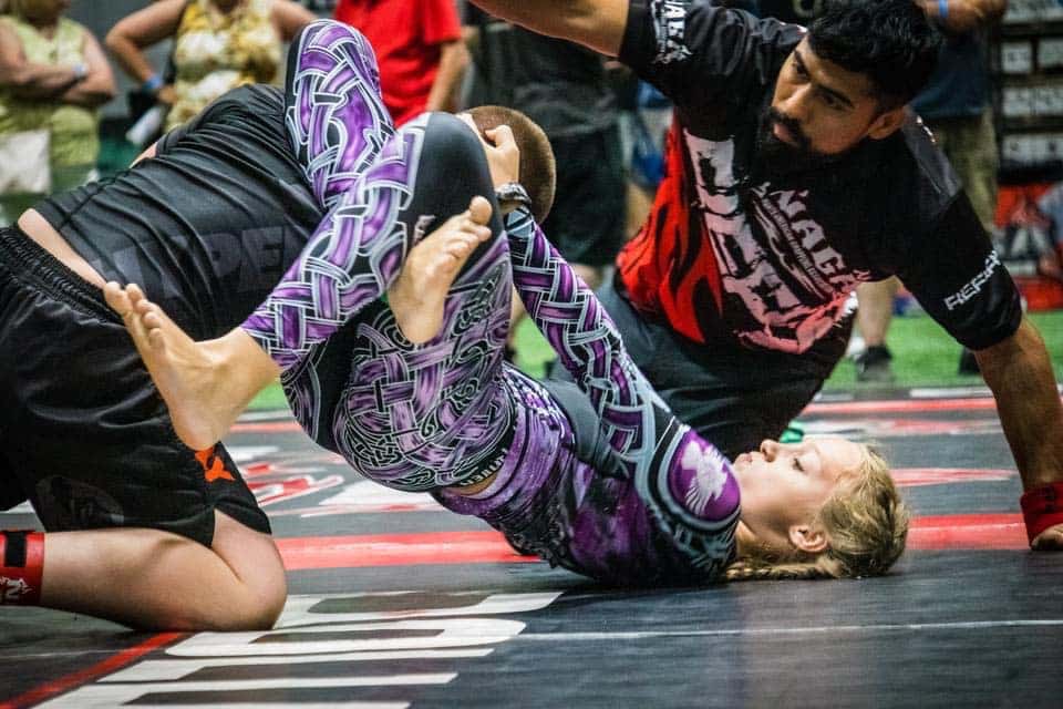 West Karate & Brazilian Jiu Jitsu students grappling on mats wearing gi uniforms.