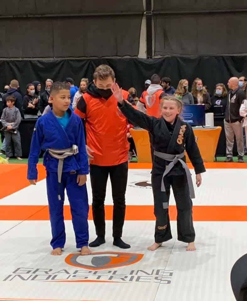 West Karate & Brazilian Jiu Jitsu young student raising hand as she wins bjj match.