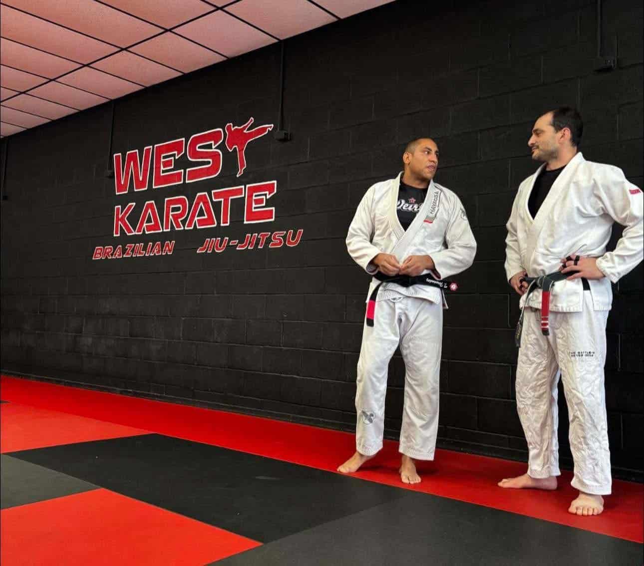 West Karate & Brazilian Jiu Jitsu instructor talking to student in front of logo on wall.
